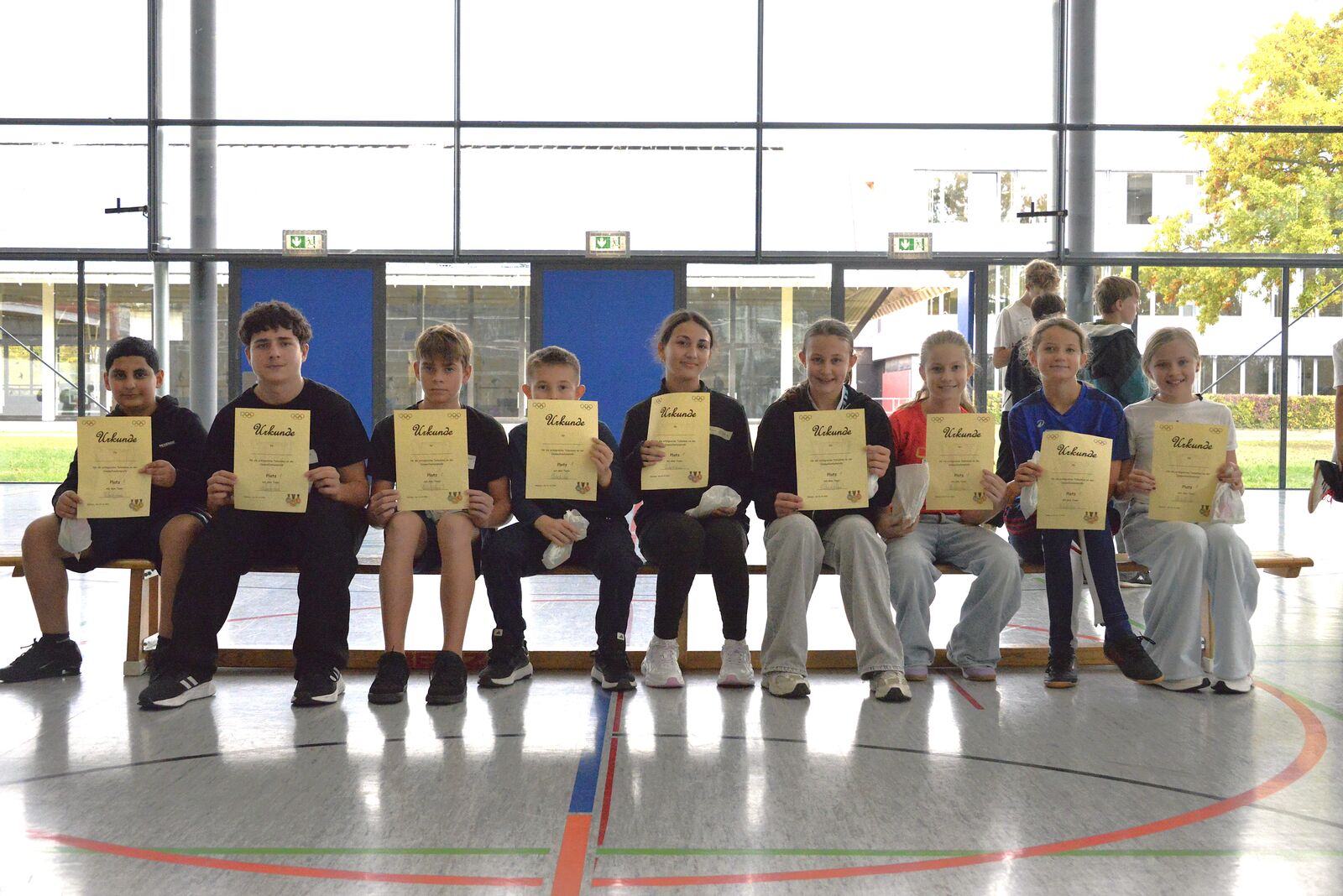 Eine Gruppe Schülerinnen und Schüler sitzt auf einer Bank und hält Urkunden in die Kamera.